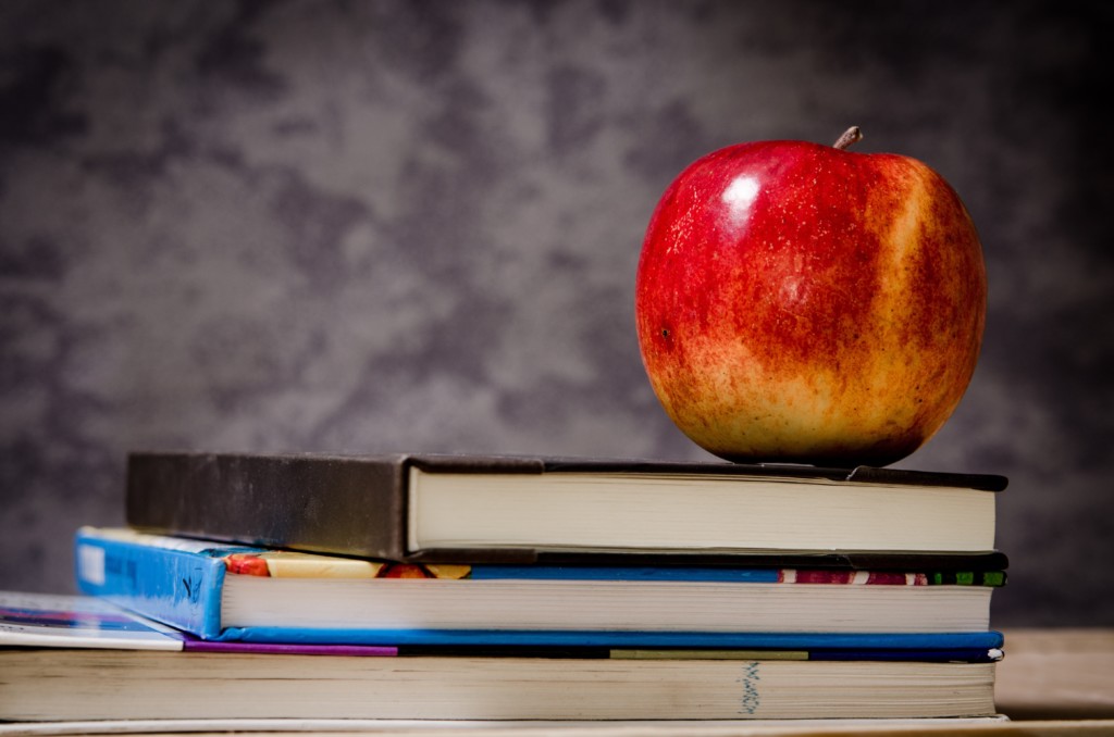 A teachers' apple and some school books, stacked on a desk.