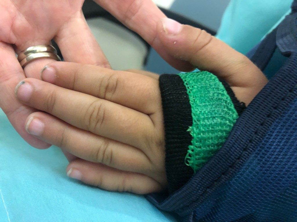 Image: A child with a broken arm holds his mom's hand