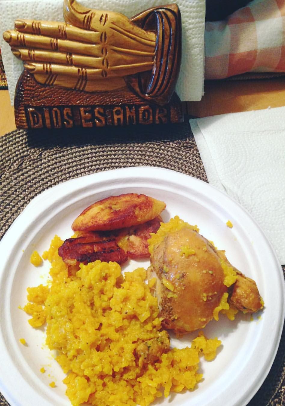 Image: A plate of arroz con pollo, maduros, and a napkin holder that says "Dios es amor"