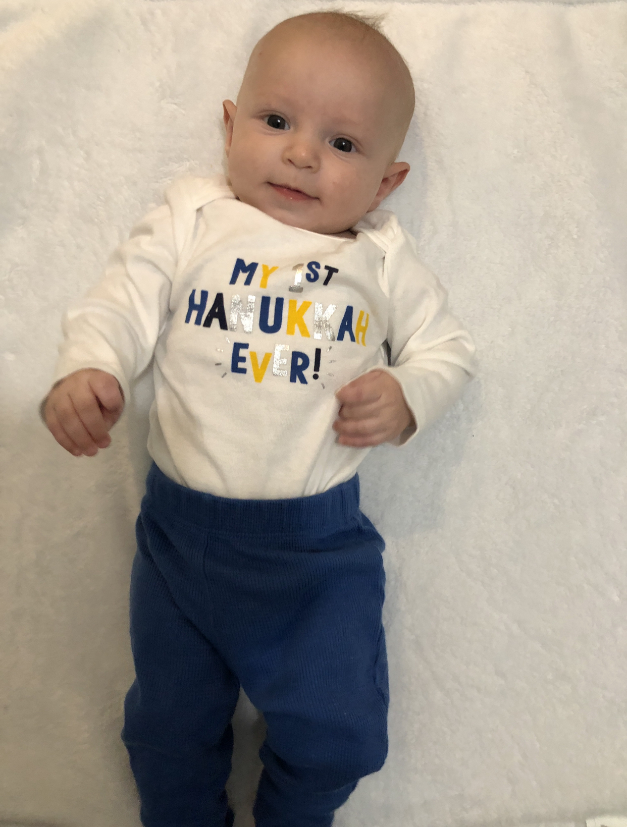 Image: An infant with a onesie that reads, "My 1st Hanukkah Ever!"