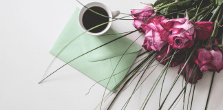 Image: A sealed envelope on a table with a cup of coffee and bouquet of roses