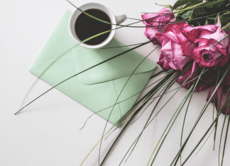 Image: A sealed envelope on a table with a cup of coffee and bouquet of roses