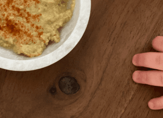 A toddler's hand reaching for a bowl of hummus