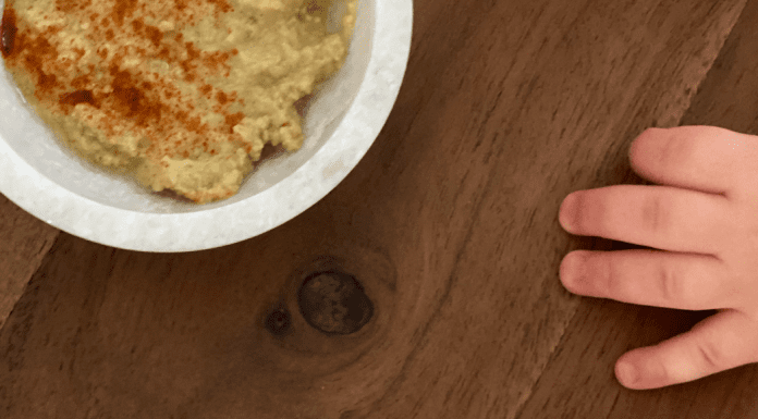 A toddler's hand reaching for a bowl of hummus