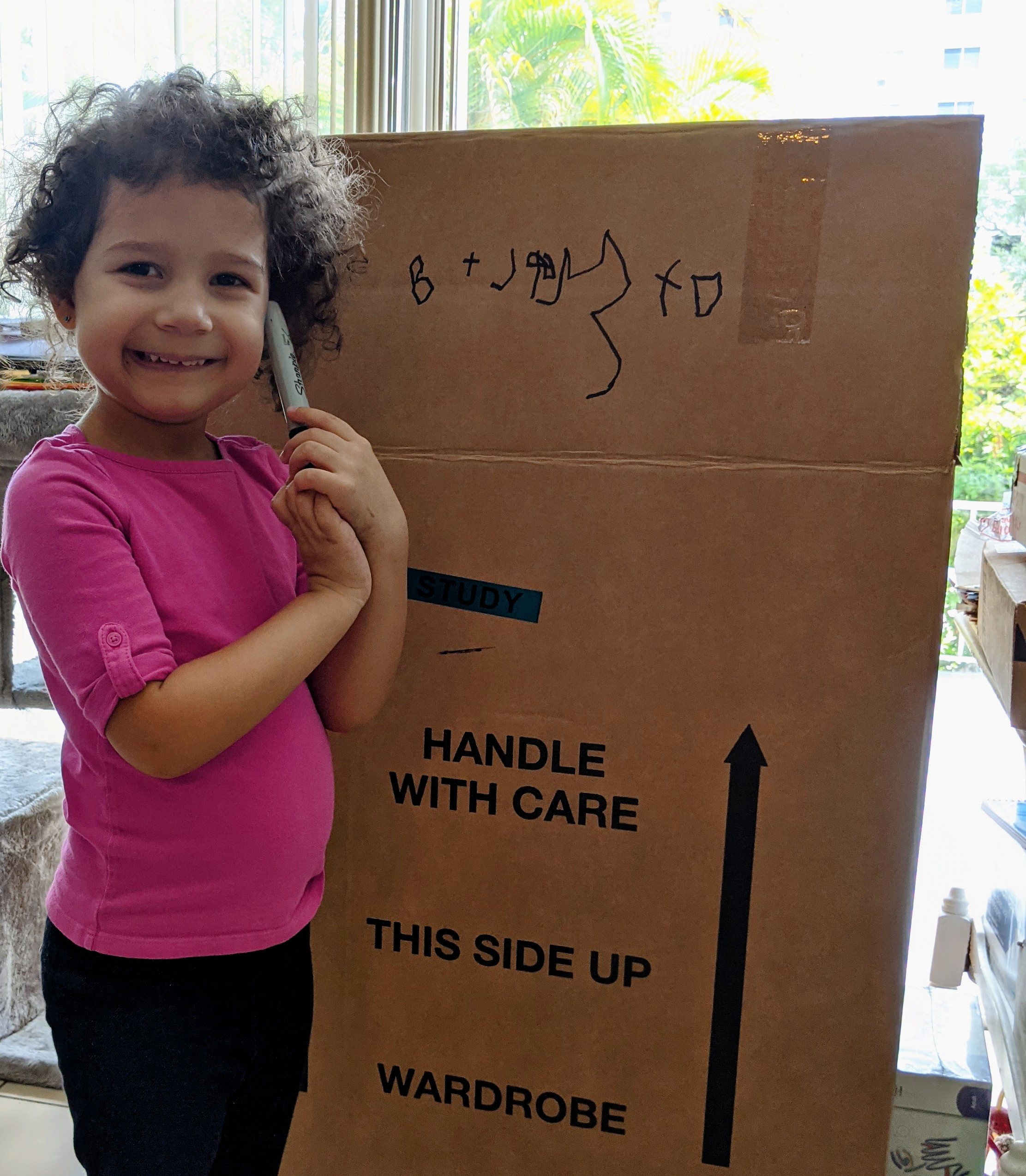 Lynda's daughter smiling next to a moving box (Dental Emergencies: Keep Calm & Call Dr. Bob Lynda Lantz Contributor Miami Mom Collective)