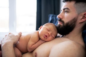 Image description: a newborn sleeping on a father's chest. (Tummy Time Without Tears: Tips From a Pediatric Physical Therapist Brittany Aquart Contributor Miami Mom Collective)