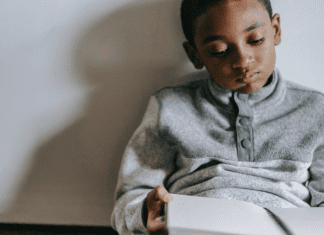 Image: A boy sitting with a book in his lap (Stuck Inside? Try These Gross Motor Games! Brittany Aquart Contributor Miami Mom Collective)
