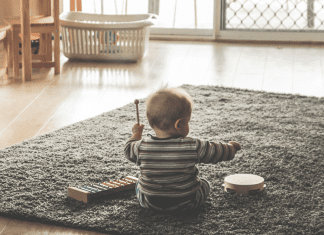 A baby playing on a grey rug in a minimalist room. The baby is playing with musical toys.