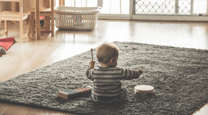 A baby playing on a grey rug in a minimalist room. The baby is playing with musical toys.