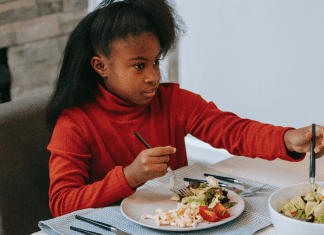 Image: A school-aged girl sitting at a table eating (Raising a Diverse Eater: 3 Keys to Success Dina Garcia Contributor Miami Mom Collective)