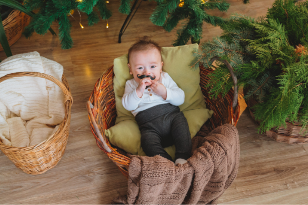 A baby boy sits propped up on some pillows in a basket