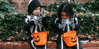 Image: Two girls in skeleton costumes sitting with their Halloween buckets