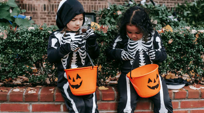 Allergy-Friendly Halloween: Tricks and Treats Image: Two girls in skeleton costumes sitting with their Halloween buckets