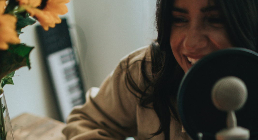 Image: A woman hosting a podcast (Listening for My Sanity: My Top 10 Podcasts Alisa Britton Contributor Miami Mom Collective)