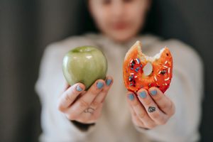 Image: A woman holding an apple in her right hand and a donut in her left (Zoe Costa Contributor Miami Mom Collective)