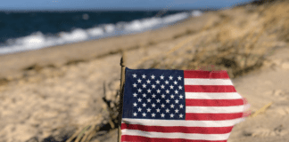 Image: An American flag in the sand with the ocean behind it