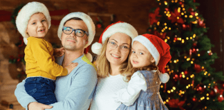 Image; A family wearing Santa hats and standing in front of a Christmas tree (Healthy Holidays: A Survival Guide | Part 2 Dina Garcia Contributor Miami Mom Collective)