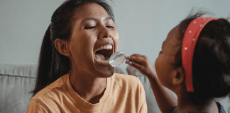 A young girl plays dentist with her mom, holding a magnifying glass up to check her teeth