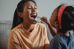 A young girl plays dentist with her mom, holding a magnifying glass up to check her teeth