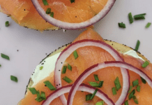 A sliced bagel topped with cream cheese, nova, and sliced red onions