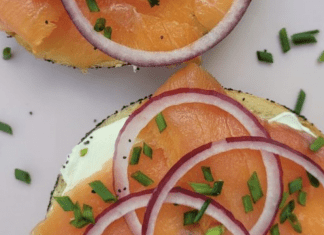 A sliced bagel topped with cream cheese, nova, and sliced red onions