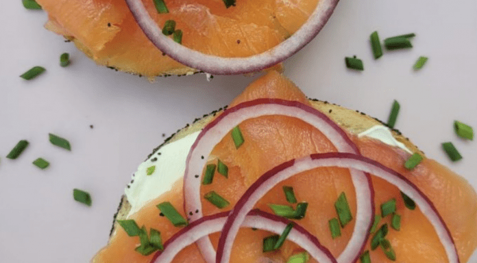 A sliced bagel topped with cream cheese, nova, and sliced red onions