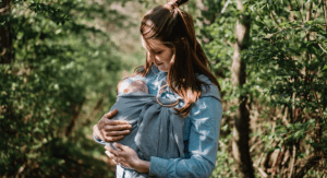 A postpartum mom wearing her newborn baby in a sling