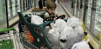 A little boy sits in shopping cart full of frozen turkeys