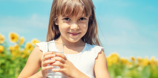 Image: A little girl holds a glass of tap water with a sunflower field in the background