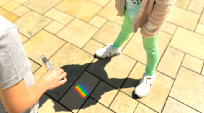 Image: Students use a prism outdoors to cast a rainbow on stone pavers