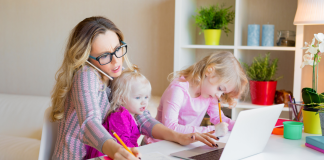 Working Mom Dilemma: Finding Balance in a Fast-Paced World Image: A working mom trying to work from home with a toddler on her lap and a preschooler next to her