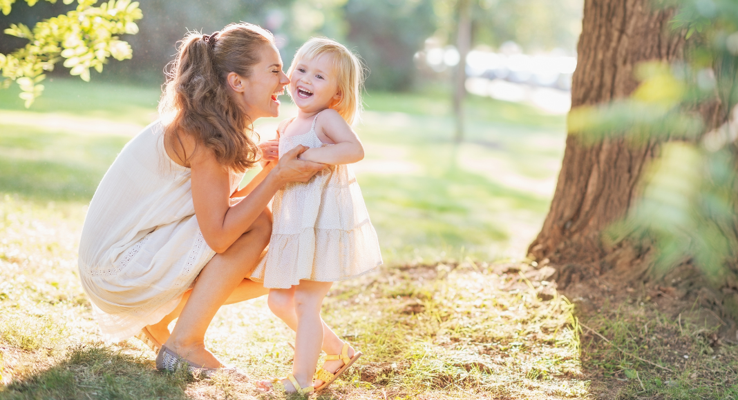Image: A mom plays with her toddler-aged daughter outdoors in the summertime