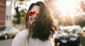 Image: A confident woman wearing sunglasses and smiling as she crosses the street