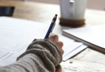 Image: Someone sitting at a desk with a pen in their hand and a cup of coffee in the background