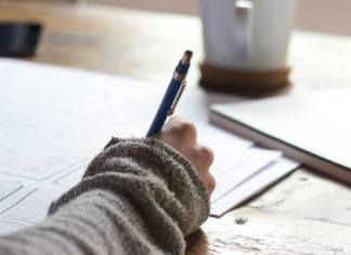 Image: Someone sitting at a desk with a pen in their hand and a cup of coffee in the background