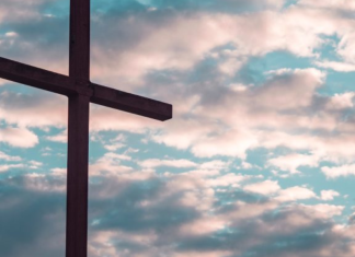 Image: A large cross silhouetted against a cloudy daytime sky