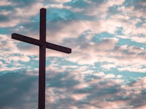 Image: A large cross silhouetted against a cloudy sky