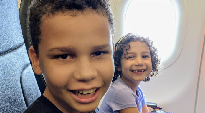 Image: Two kids smiling from their seats on an airplane