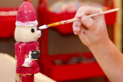 Elf Factory 2025 Holiday Guide Graphic Image: A child paints a Santa figure at Elf Factory