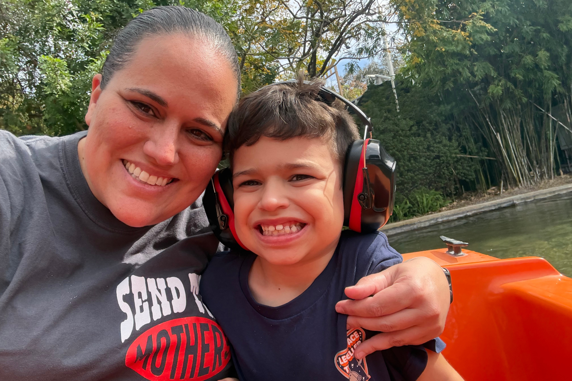 An autism mom has her arm around her son who is wearing autism sensory headphones. They are in an orange small boat in the water.