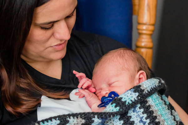 A new mom is holding a newborn baby boy wrapped in a blue crocheted blanket close against her chest.